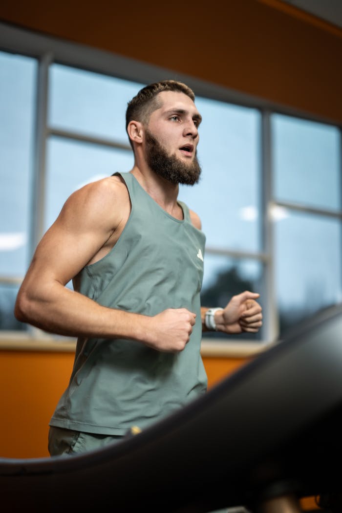 services-03 Focused young man jogging on a treadmill in a modern gym with large windows.